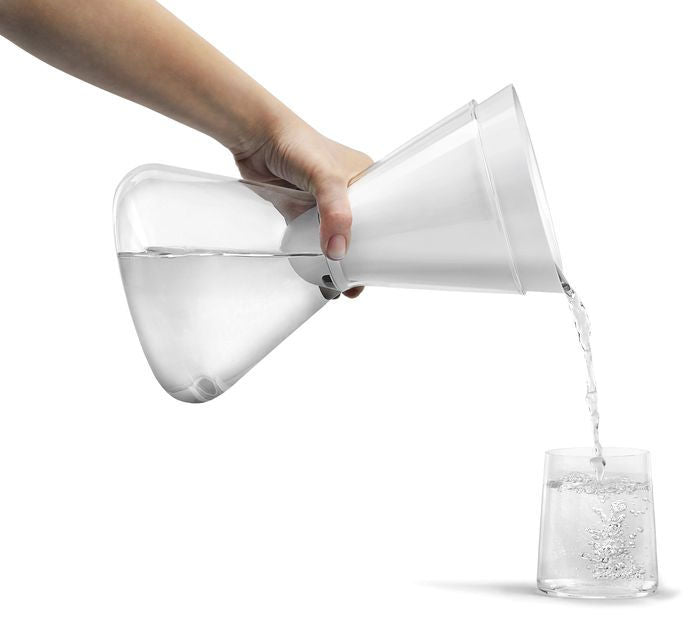 Clear glass carafe being filled with water from a white pitcher on a white background