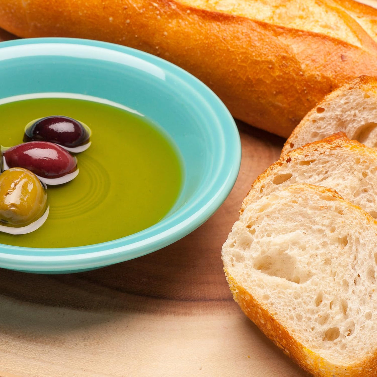 Sliced bread with a bowl of olive oil and olives on a wooden surface