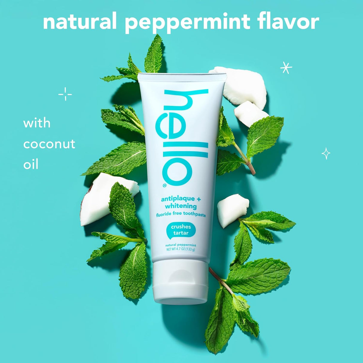 Tube of 'hello' toothpaste with peppermint leaves and coconut pieces on a blue background