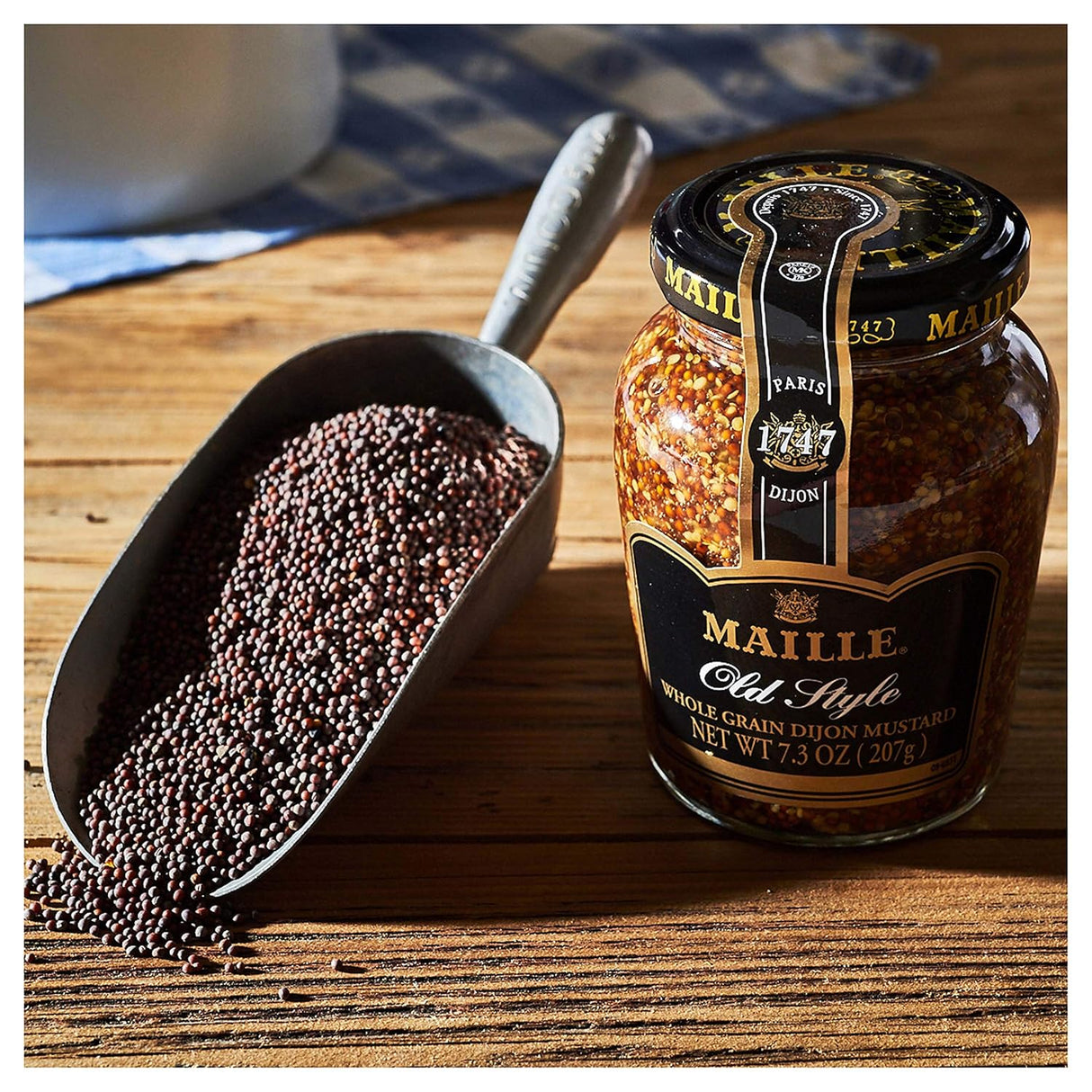 Maille whole grain dijon mustard jar with a scoop of mustard seeds on a wooden surface.