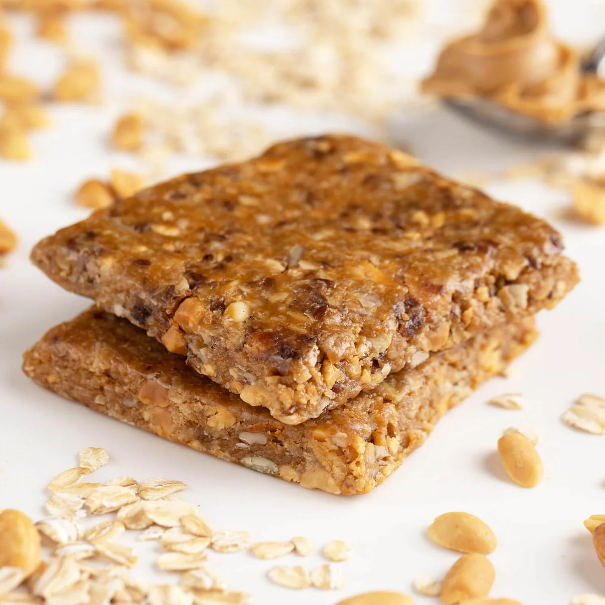 Pro Bar Meal on-the-go peanut butter bar: Two granola bars stacked on a white surface with oats and peanuts scattered around
