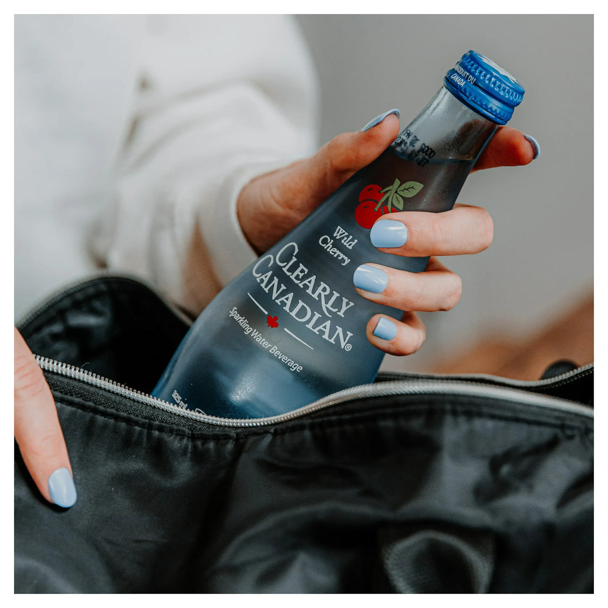 Hand holding a 'Clearly Canadian' sparkling water bottle with a cherry label.
