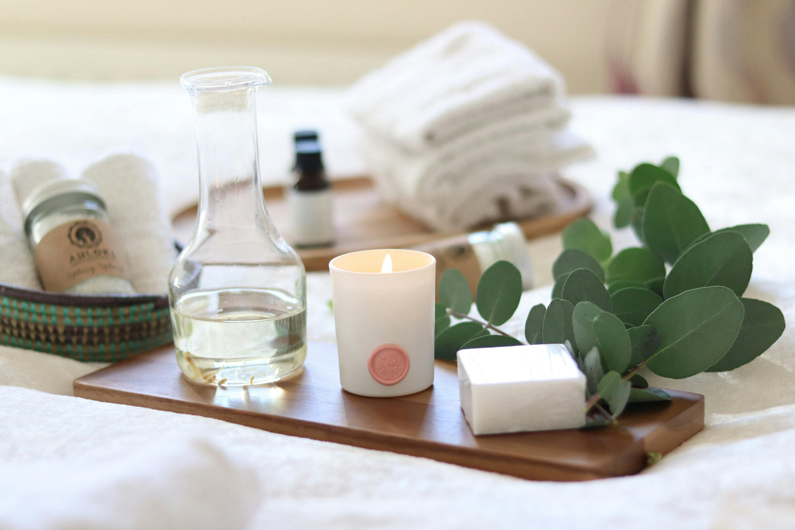 Bathroom setting with a candle, soap, and eucalyptus leaves on a wooden tray.