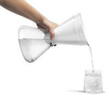 Clear glass carafe being filled with water from a white pitcher on a white background