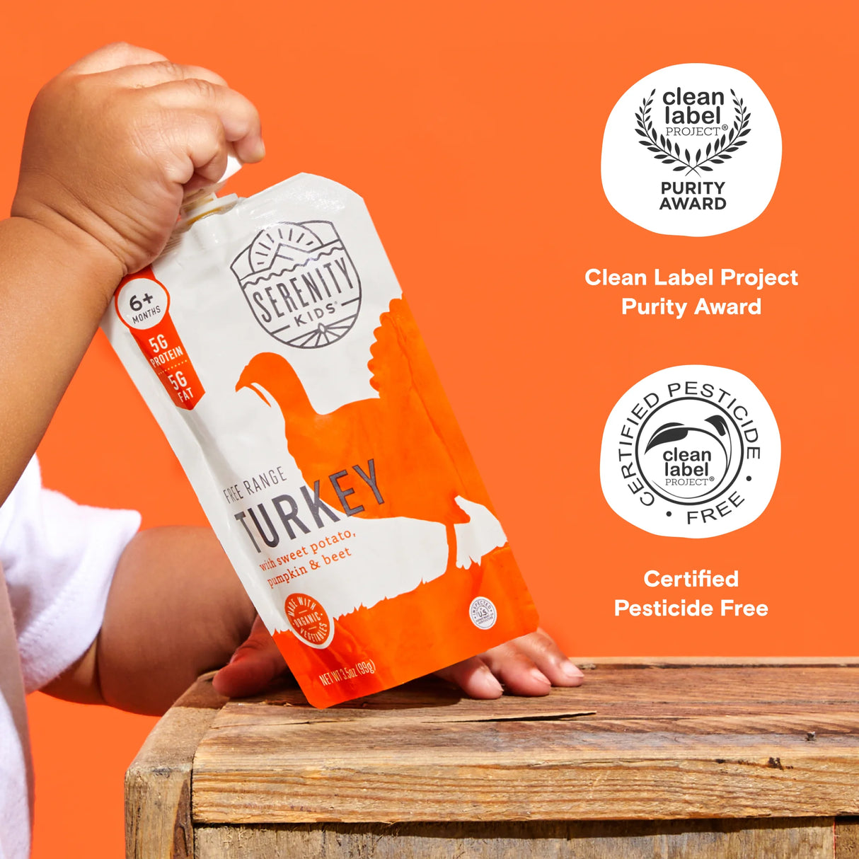 Child's hand holding a Serenity Kids turkey package against an orange background with Clean Label Project awards displayed.