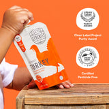 Child's hand holding a Serenity Kids turkey package against an orange background with Clean Label Project awards displayed.