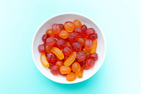 White bowl filled with colorful gummy candies on a light blue background
