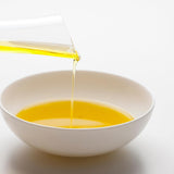 olive oil being poured from a glass container into a white bowl on a white background