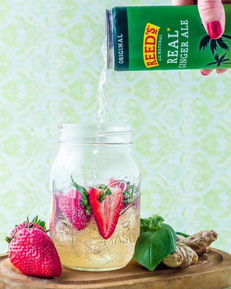 Reed's Real Ginger Ale being poured into a glass with strawberries and basil on a green background