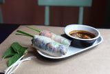 Spring rolls with a dipping sauce on a white plate on a wooden table.