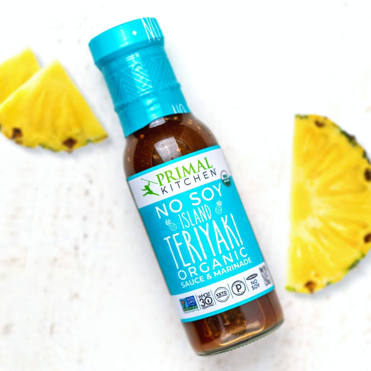 Bottle of Primal Kitchen No Soy Island Teriyaki Organic Sauce & Marinade with pineapple slices on a white background