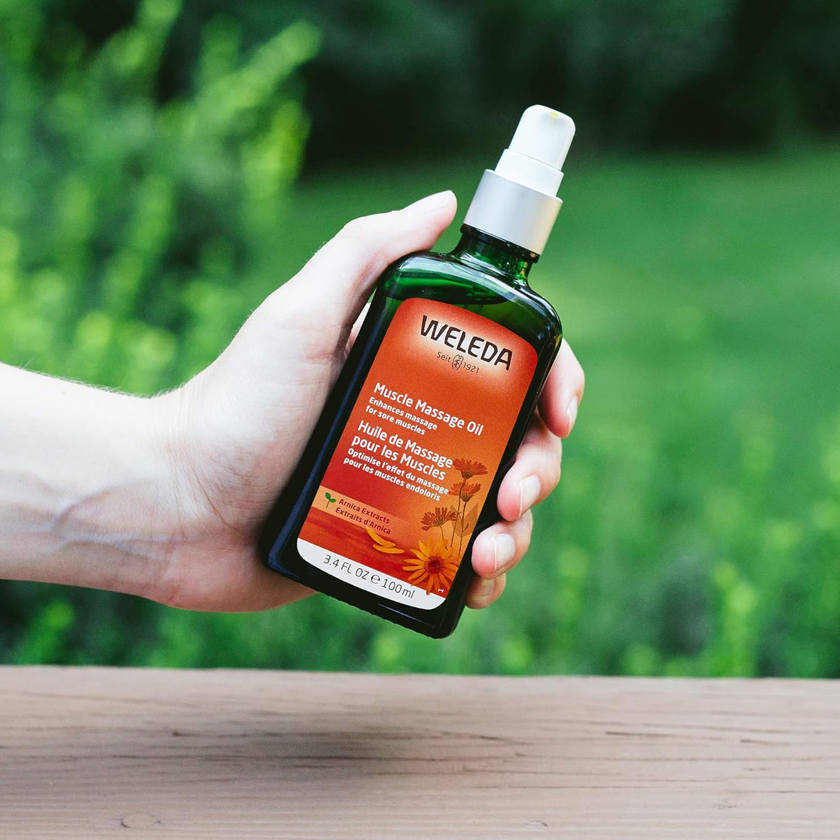 Hand holding a Weleda muscle massage oil bottle with a green blurred background