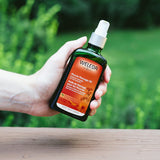 Hand holding a Weleda muscle massage oil bottle with a green blurred background