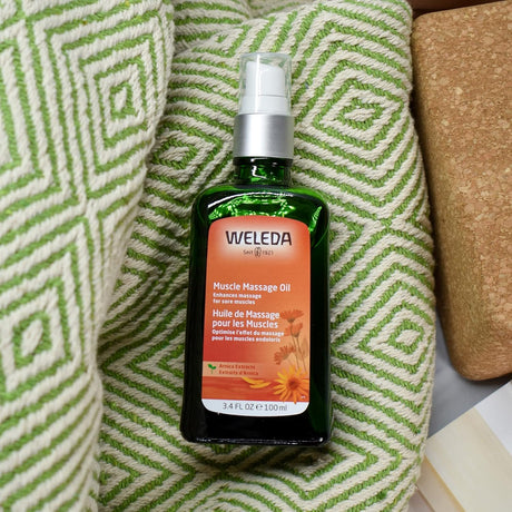 Weleda muscle massage oil bottle on a textured green and white surface