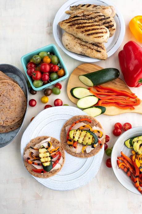 Plates of food with grilled chicken, vegetables, and flatbreads on a light background