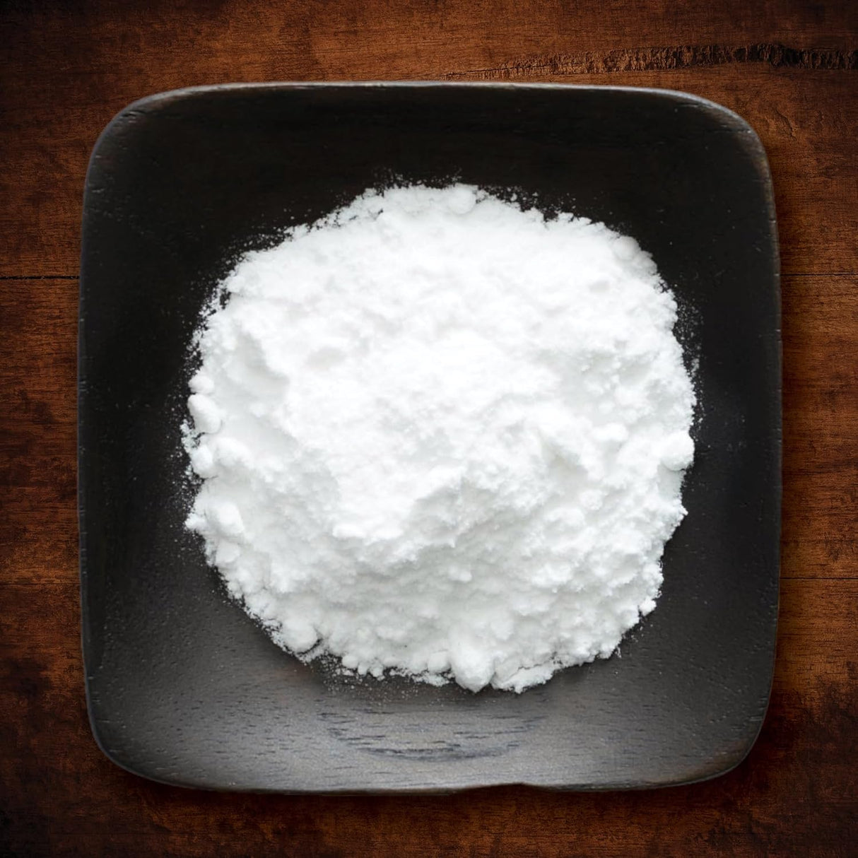 White powdery substance in a black square bowl on a wooden surface