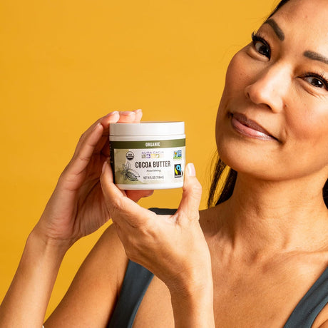 Woman holding a jar of organic cocoa butter against a yellow background