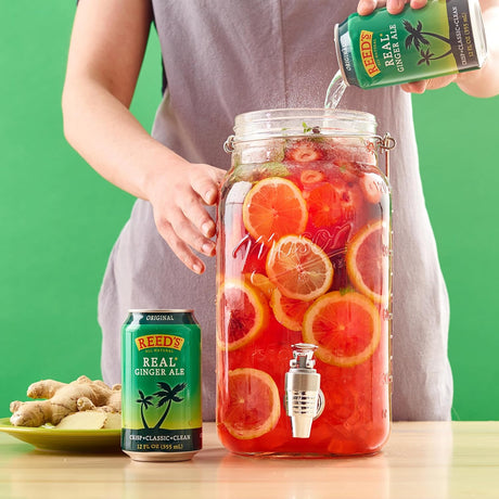 Person pouring Reedy's Real Ginger Ale into a glass jar filled with fruit slices on a green background.