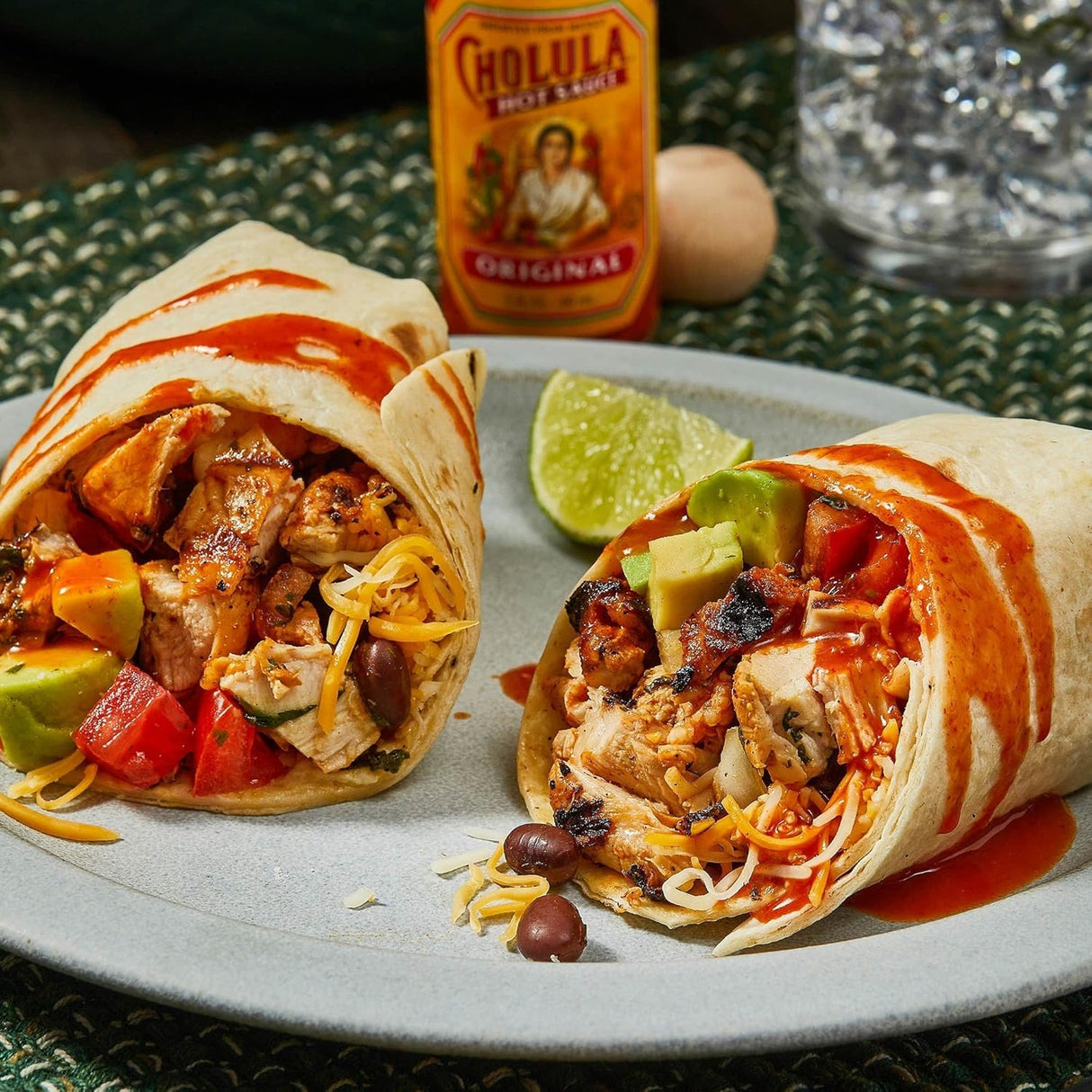 Colorful burrito with chicken, vegetables, and Cholula hot sauce on a plate.