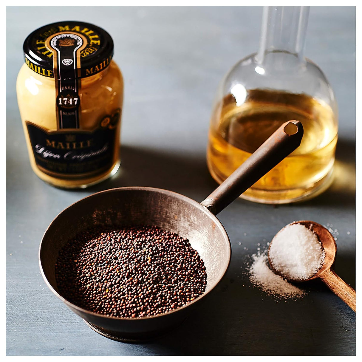 Jar of Malle, bowl of seeds, and spoon with salt on a gray surface