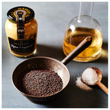 Jar of Malle, bowl of seeds, and spoon with salt on a gray surface