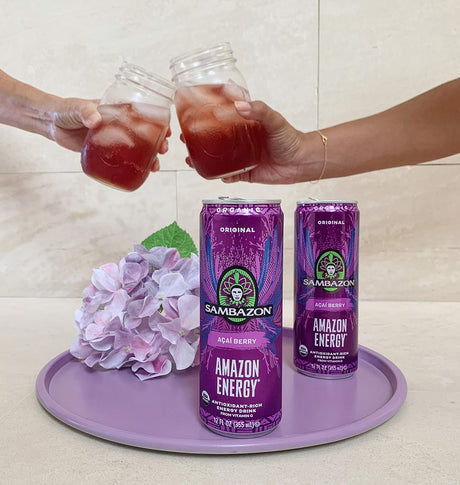 Two hands holding glasses of a red beverage with Sambazon Amazon Energy drinks on a tray.