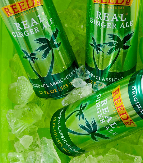 Three bottles of Reed's Real Ginger Ale on a green background with ice cubes.