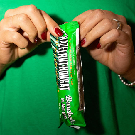 Person opening a green Barebells Nutendoat protein bar against a green background
