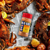 Old Bay seasoning bottle surrounded by crabs and potatoes on a newspaper background