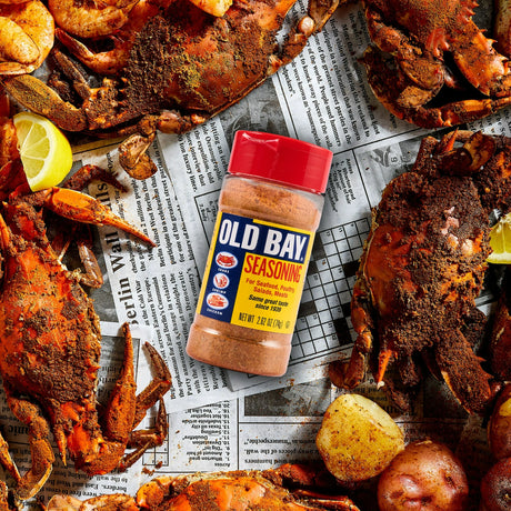 Old Bay seasoning bottle surrounded by crabs and potatoes on a newspaper background