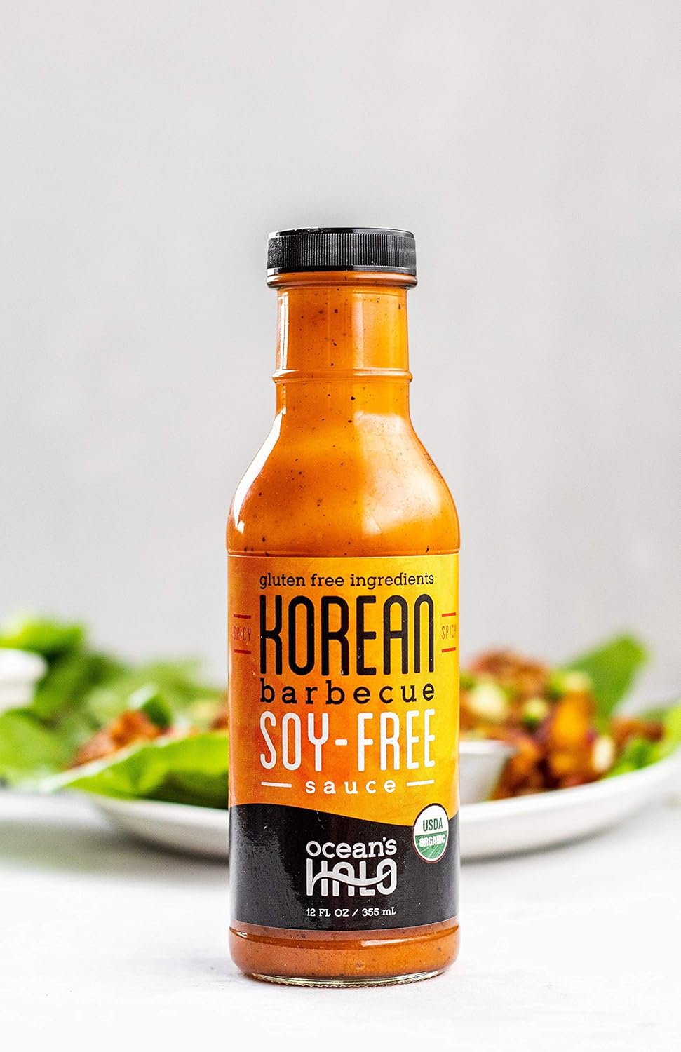 Bottle of Korean barbecue soy-free sauce on a white background with blurred salad and dish in the background.