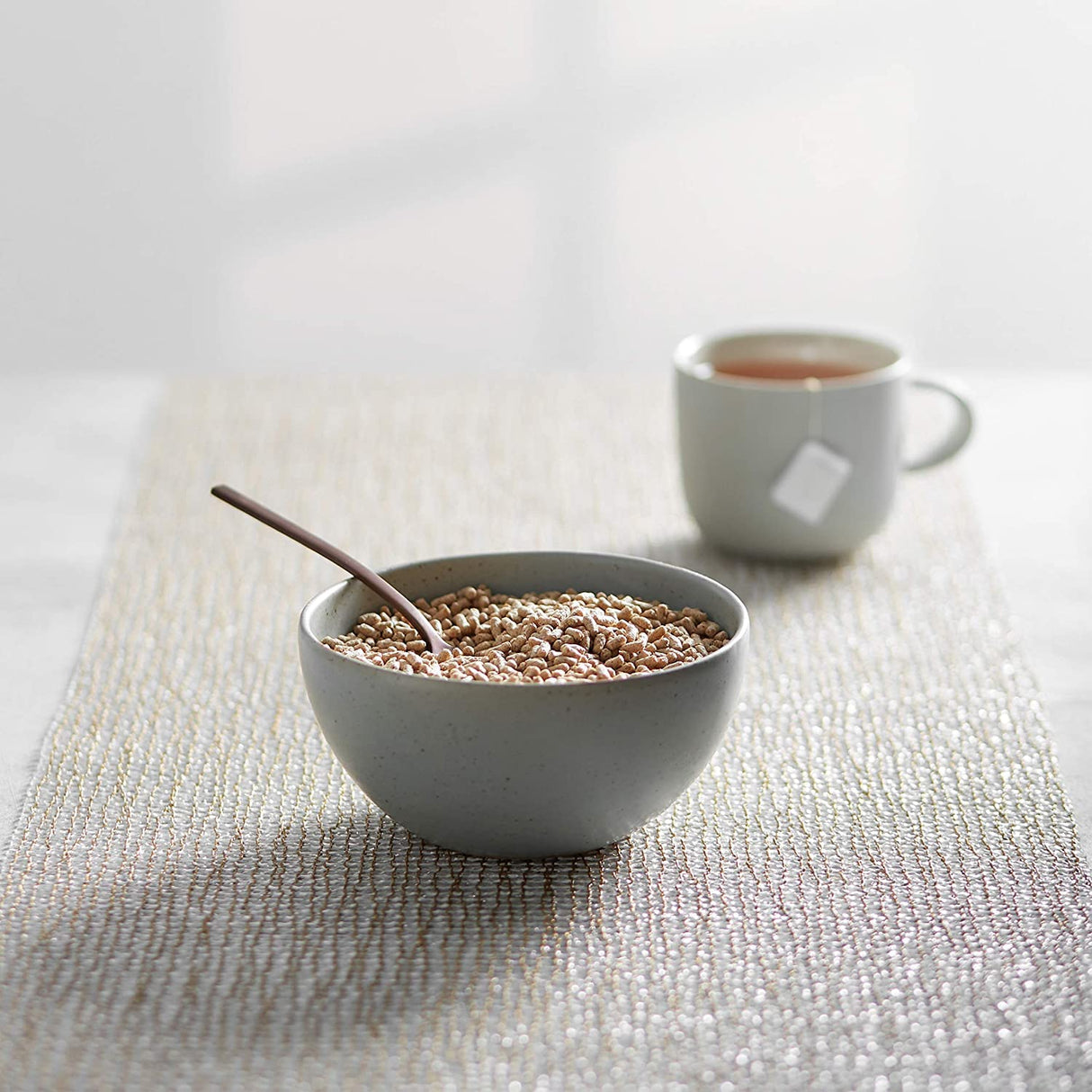Bowl of cereal with a spoon and a cup of tea on a textured surface