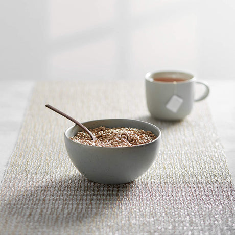 Bowl of cereal with a spoon and a cup of tea on a textured surface