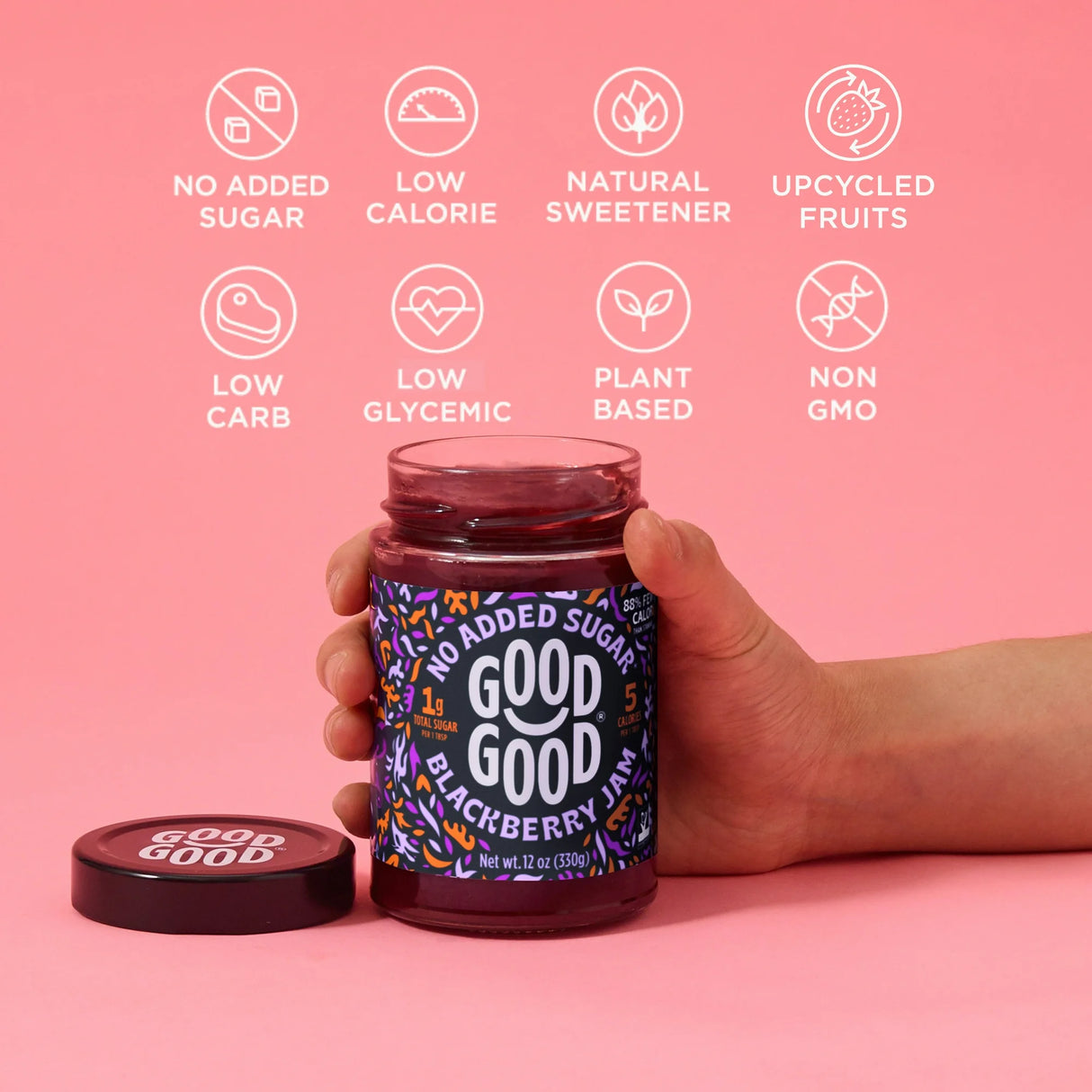 Hand holding a jar of 'Good Good' blackberry jam with health benefits icons on a pink background