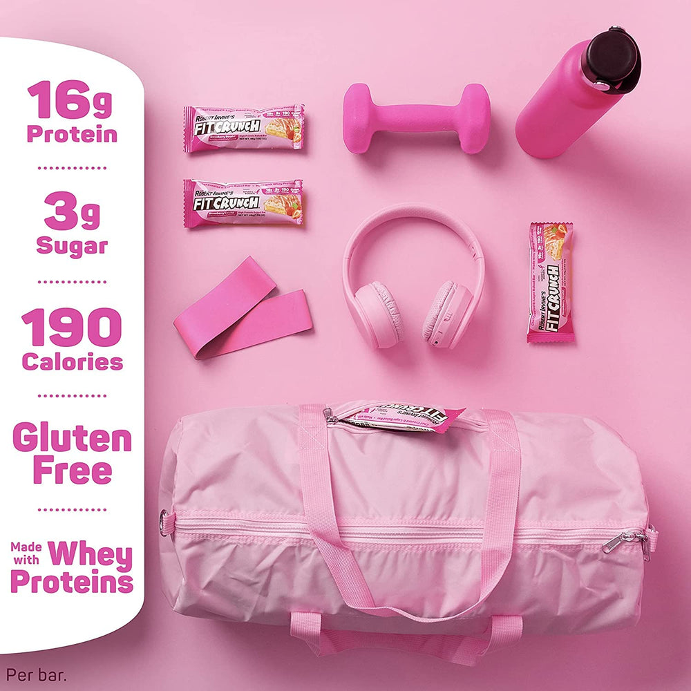 Pink gym bag with fit crunch protein bars, dumbbells, headphones, and a water bottle on a pink background.