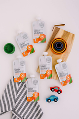 Pouches of 'Turkey Bolognese' on a white background with a wooden board and small toys.