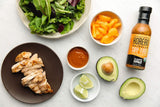 Salad ingredients including chicken, avocado, and a bottle of soy-free barbecue sauce on a white surface.