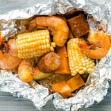  foil packet with shrimp, corn, and sausage on a wooden surface